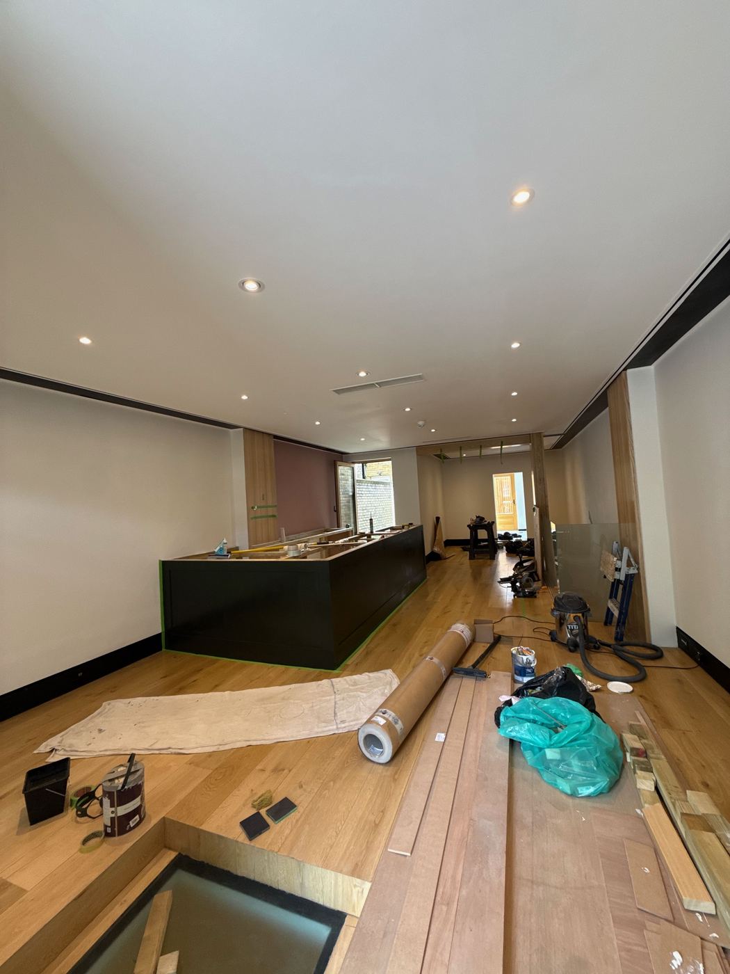 The café mid-build — oak floors, dusty-rose wall, dark counter